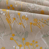Gros plan sur le tissu brodé de motifs végétaux au mètre de Longan Craft France, qui présente des broderies florales jaunes, blanches et vert pâle avec des coutures complexes - idéal pour les vêtements, les accessoires et la décoration.