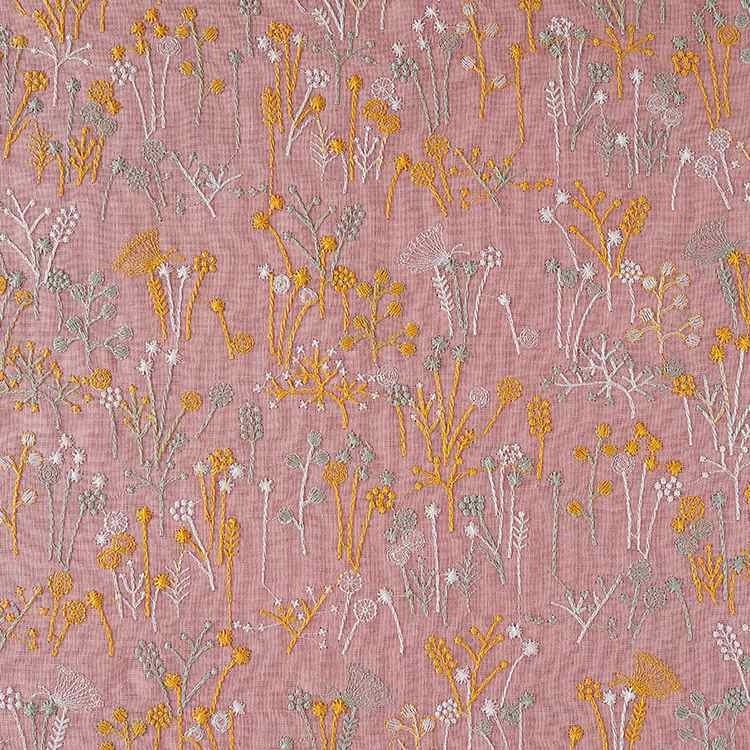 Le tissu brodé de motifs végétaux au mètre Longan Craft France, avec fleurs et plantes jaunes, blanches et grises sur fond rose poudré, est idéal pour vêtements, accessoires ou décoration.