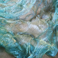 Gros plan sur un tissu bleu, translucide et ondulé fabriqué à partir de Tissu organza irisé plissé au mètre-bicolore transparent à dégradé par Longan Craft France. La surface brillante et texturée ressemble à de l'eau qui coule.
