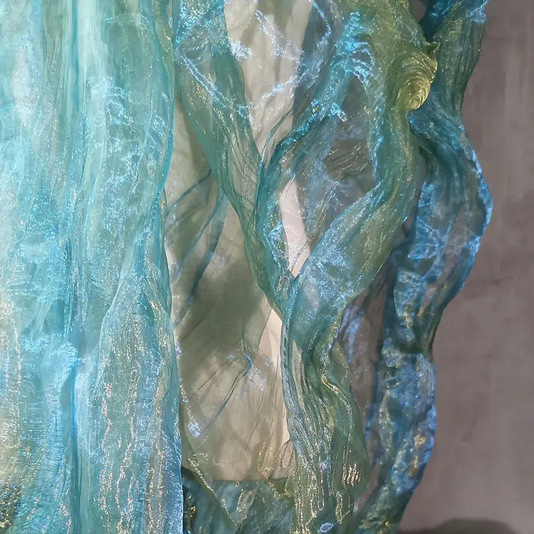 Gros plan sur Tissu organza irisé plissé au mètre de Longan Craft France : panneaux semi-transparents, bicolores à dégradé en bleu pâle et vert, superposés verticalement avec des effets de lumière chatoyants et fluides.