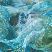 Gros plan sur Tissu organza irisé plissé au mètre de Longan Craft France : tissu bicolore transparent à dégradé dont la texture brillante et froissée crée des effets de vagues bleues et turquoises.