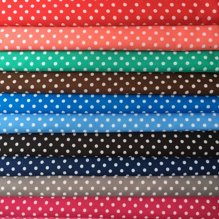 Une pile de Longan Craft France tissu peau de pêche imprimé à pois au mètre en microfibre polyester rouge, corail, vert, marron, bleu, noir et gris est disposée en couches, montrant la texture douce parfaite pour les jupes.