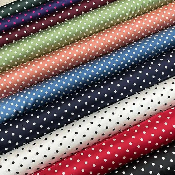 Le tissu en soie extensible à pois au mètre -soie imprimée 19 mommes avec élasthanne- de Longan Craft France présente des pois blancs sur des tissus bleu marine, vert, pêche, rose, noir, blanc et rouge disposés en diagonale.
