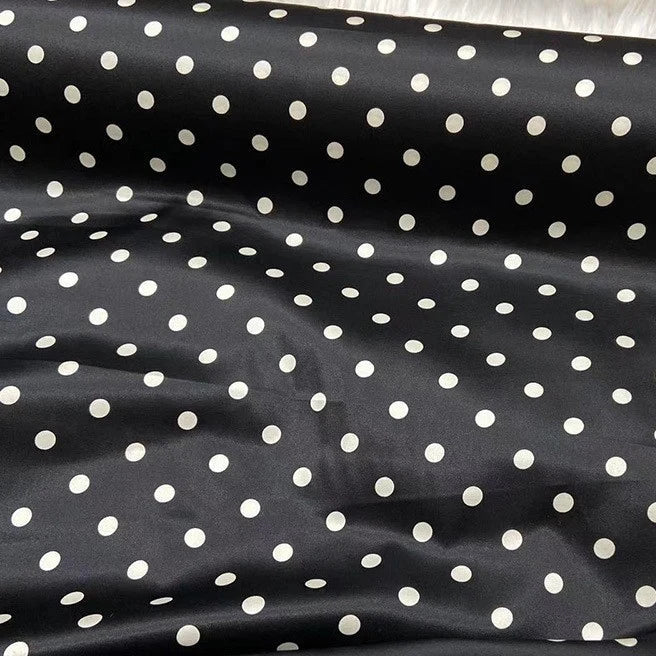 Une longueur de tissu en soie extensible à pois au mètre de Longan Craft France, une soie stretch 19 mamans à pois blancs sur fond noir, présente des plis doux et révèle l'élégance vintage de la soie de mûrier imprimée.