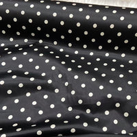 Une longueur de tissu en soie extensible à pois au mètre de Longan Craft France, une soie stretch 19 mamans à pois blancs sur fond noir, présente des plis doux et révèle l'élégance vintage de la soie de mûrier imprimée.
