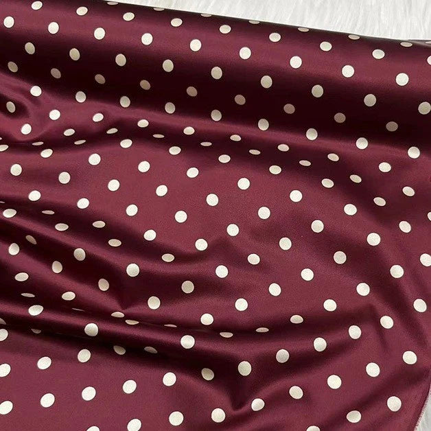 Le tissu en soie extensible à pois au mètre de Longan Craft France est une soie imprimée 19 mamans avec élasthanne, d'inspiration vintage. Il présente des pois blancs régulièrement espacés sur fond marron, une texture brillante et lisse et des plis visibles.