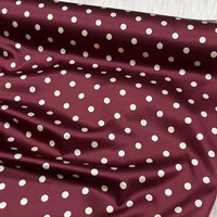 Le tissu en soie extensible à pois au mètre de Longan Craft France est une soie imprimée 19 mamans avec élasthanne, d'inspiration vintage. Il présente des pois blancs régulièrement espacés sur fond marron, une texture brillante et lisse et des plis visibles.