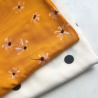 Deux tissus soigneusement pliés de Longan Craft France sont présentés : un "tissu viscose fleuri à pois" jaune moutarde avec un imprimé floral rose/noir, et un tissu blanc avec de gros points noirs régulièrement espacés. Tous deux sont 100 % viscose et conviennent parfaitement aux jupes longues à la mode.