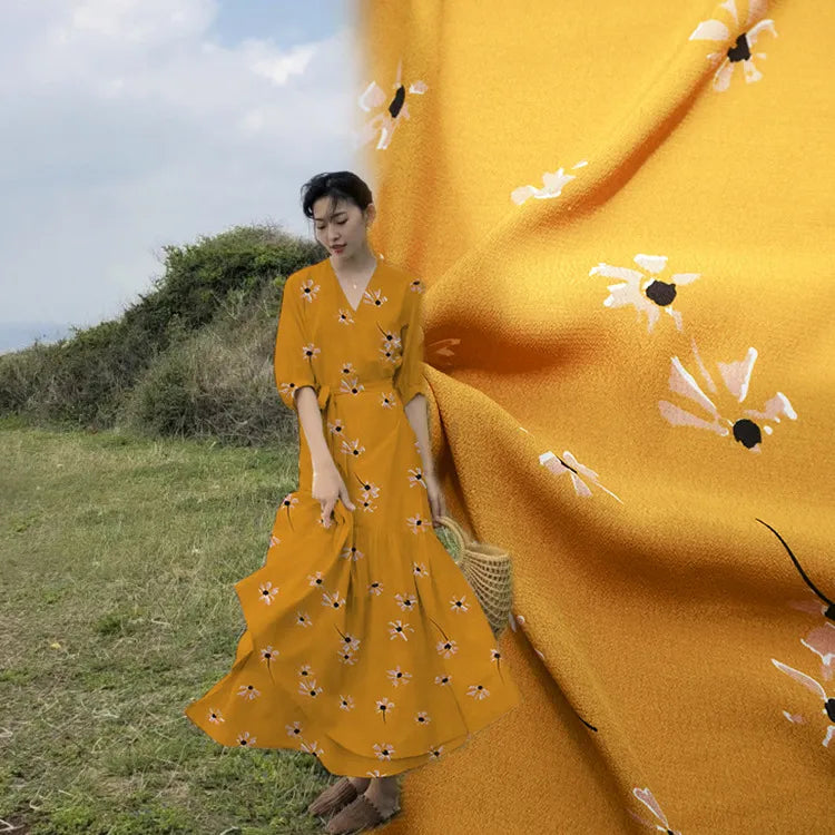 Une femme se tient à l'extérieur, vêtue d'une jupe longue en "Tissu viscose fleuri à pois au mètre" de Longan Craft France, un tissu tendance 100 % viscose aux imprimés floraux blancs et noirs sur fond jaune. Un gros plan met en évidence le motif.