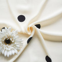 Gros plan sur le tissu viscose fleuri à pois au mètre - 100 % viscose imprimée - de Longan Craft France. Ce tissu crème est orné de gros points noirs et d'une fleur blanche - une matière tendance idéale pour les jupes longues.
