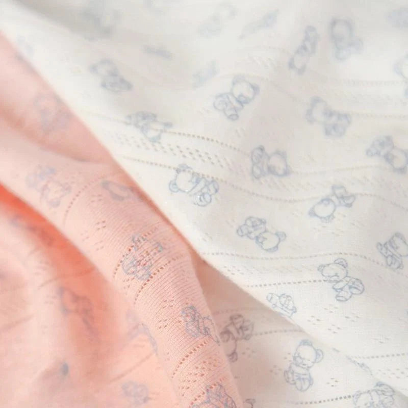 Gros plan sur le Tissu pointelle motif ours au mètre de Longan Craft France : coton ajouré rose pâle et tissu côtelé blanc à motifs d'ours bleu clair, idéal pour la confection de vêtements d'enfants, se superposant délicatement.
