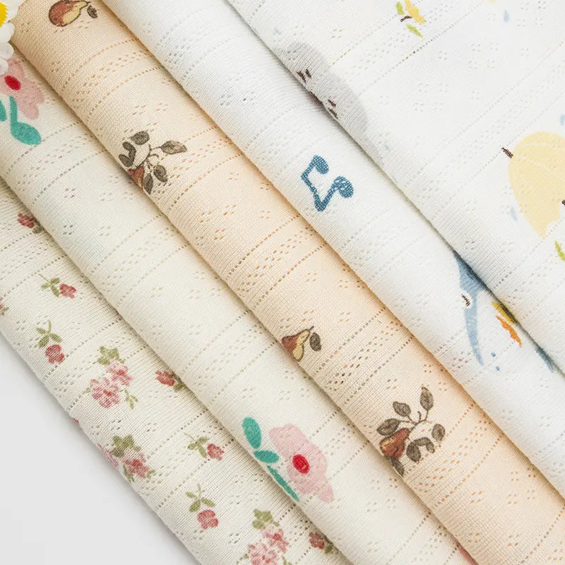Quatre pièces de Tissu pointelle en coton imprimé au mètre de Longan Craft France, présentées côte à côte, arborent des motifs floraux et animaliers pastel. Parfait pour la couture DIY de vêtements d'enfants grâce à la maille douce et texturée.