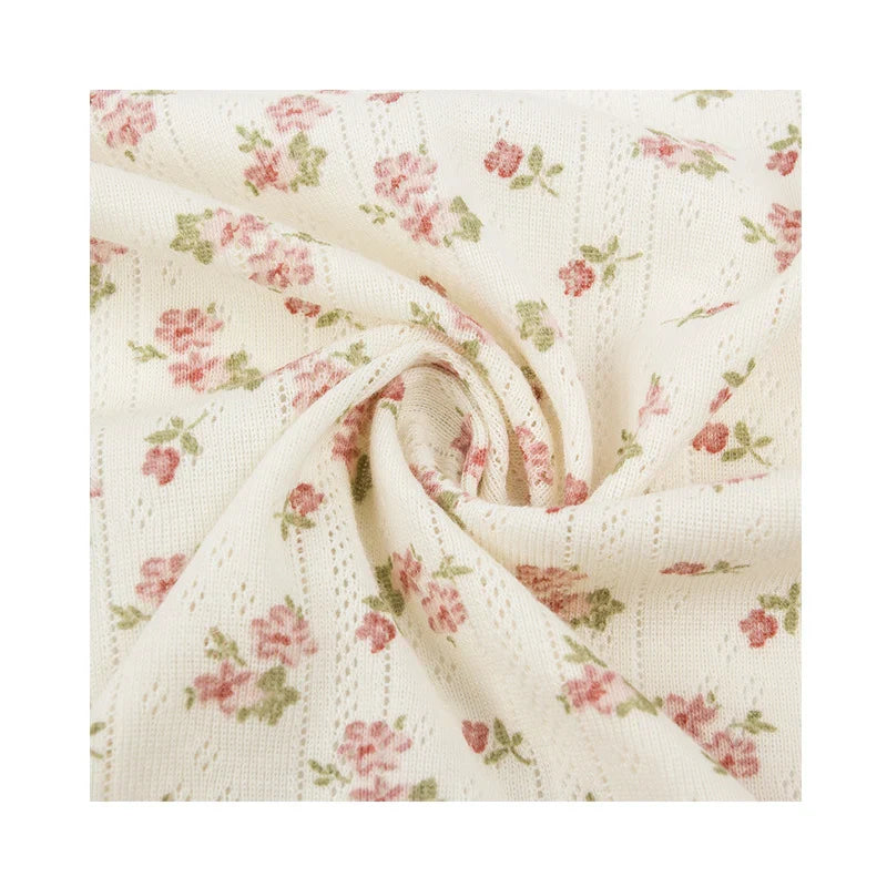 Gros plan sur le Tissu pointelle en coton imprimé de Longan Craft France - un tricot de coton crème de haute qualité avec de minuscules fleurs roses et vertes, torsadées pour montrer la texture ; un tissu idéal pour le bricolage de vêtements sûrs pour les bébés et la couture pour les enfants.