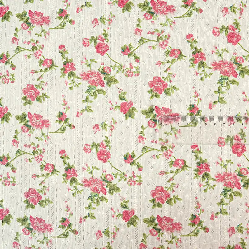 Tissu pointelle en coton imprimé au mètre de Longan Craft France : motif de roses roses et feuilles vertes sur fond crème à texture subtile. Idéal pour la couture DIY enfants. Une règle transparente en cm apparaît à droite pour l'échelle.