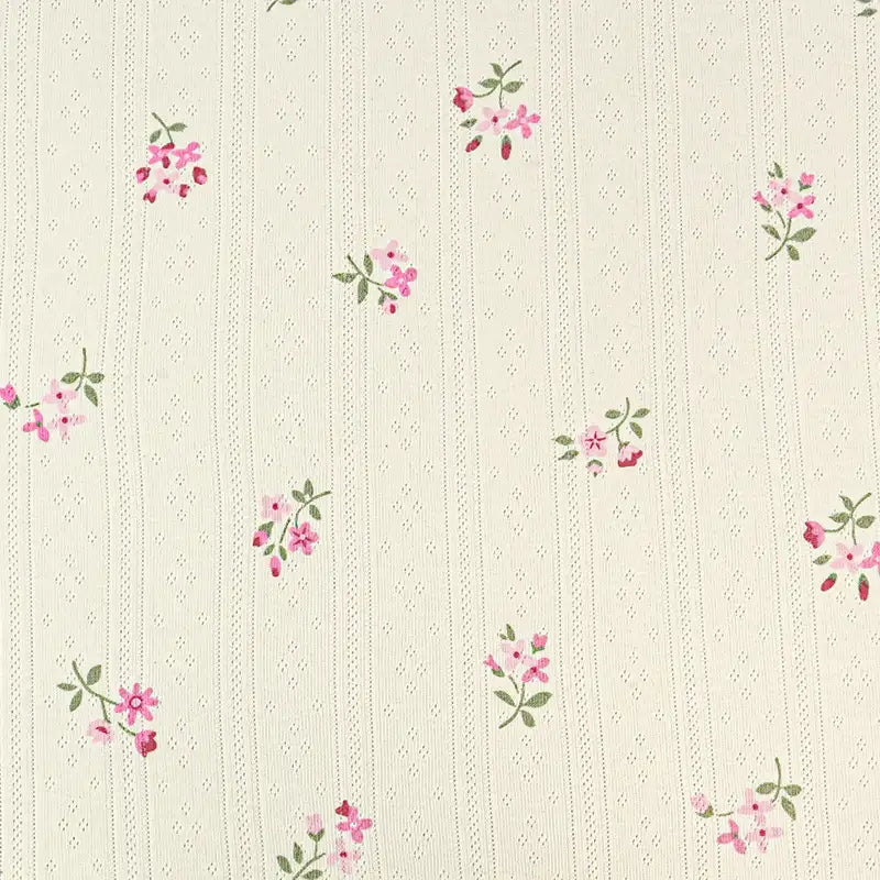 Le tissu pointelle en coton imprimé de Longan Craft France, idéal pour la couture de vêtements d'enfants, présente des lignes pointillées verticales et de petits bouquets roses avec feuilles vertes sur fond crème.