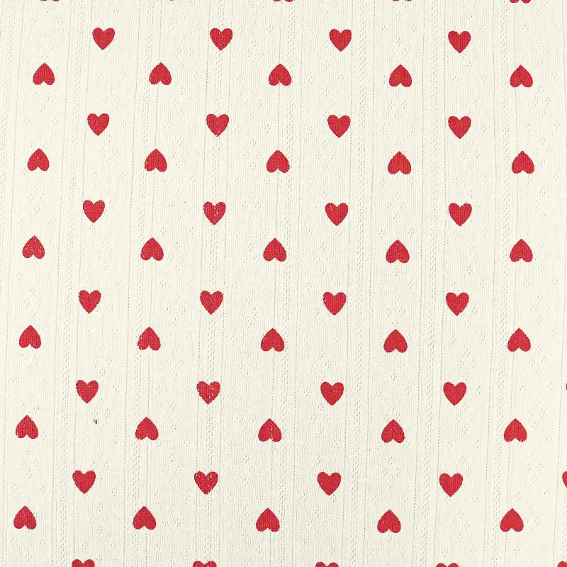 Avec un fond crème et des cœurs rouges, le Tissu pointelle en coton imprimé au mètre de Longan Craft France est un tricot de haute qualité, idéal pour coudre de jolis vêtements d'enfants et de bébés.