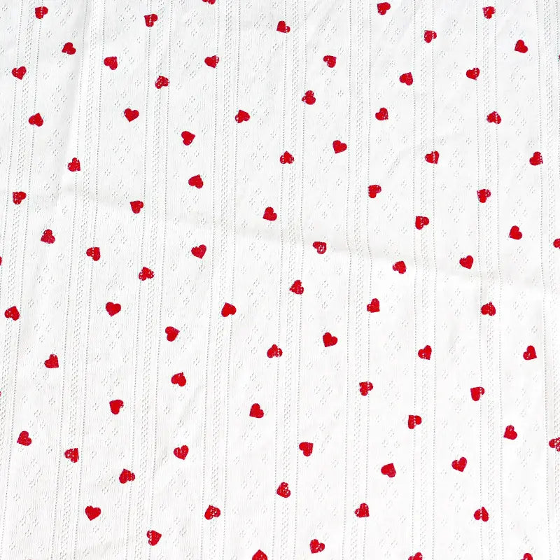 Le Tissu pointelle en coton imprimé au mètre de Longan Craft France est un tricot de coton de haute qualité avec des petits cœurs rouges et de subtiles lignes verticales en pointillés. C'est le matériel idéal pour les vêtements d'enfants et les projets de couture.