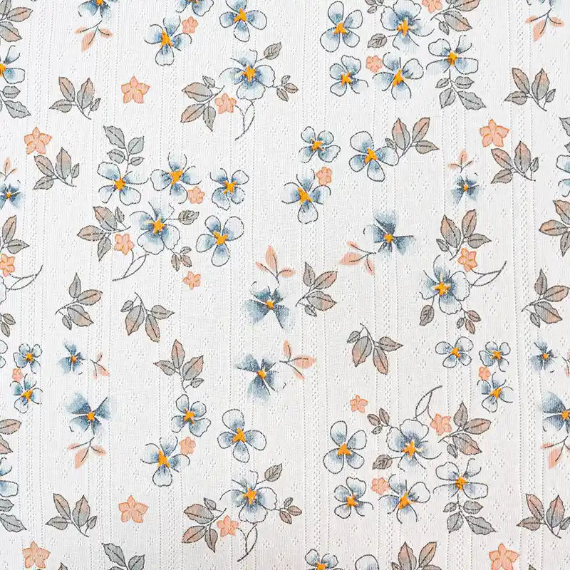 Tissu pointelle en coton imprimé de Longan Craft France : un tissu maille à fleurs bleues, jaunes, orange et feuilles brunes sur fond blanc, idéal pour la couture de vêtements d'enfants grâce à son motif régulier.