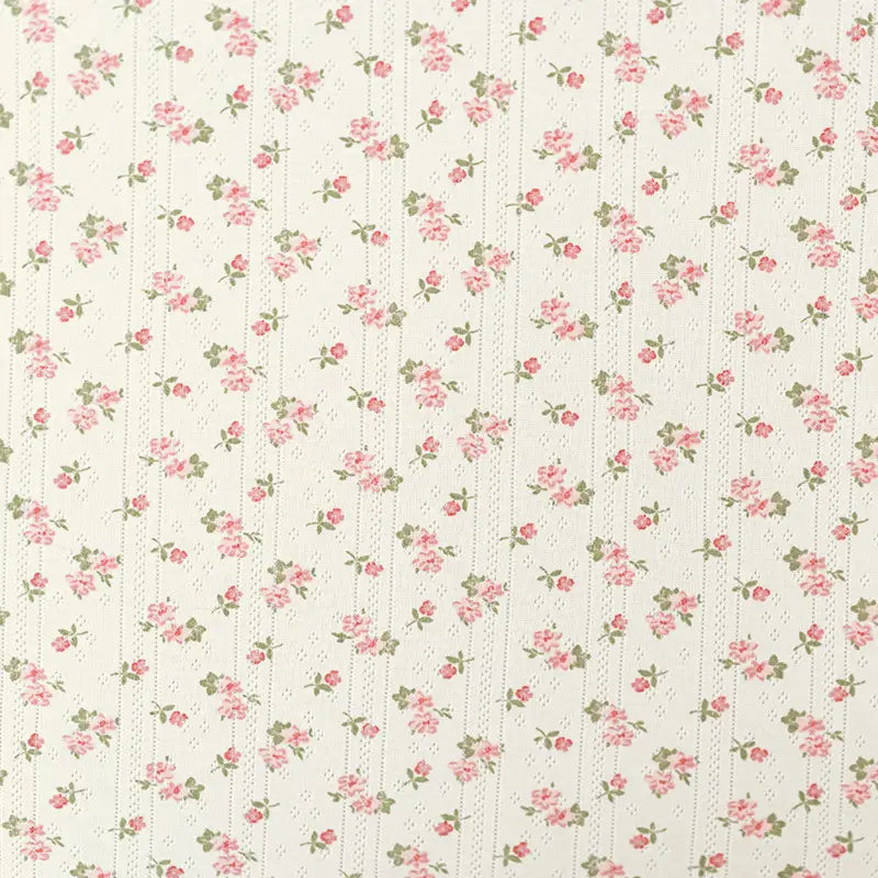 Le "Tissu pointelle en coton imprimé au mètre" de Longan Craft France est un tissu en coton crème avec de petites roses roses et des feuilles vertes dans d'élégantes rayures verticales, parfait pour le bricolage de vêtements pour enfants.