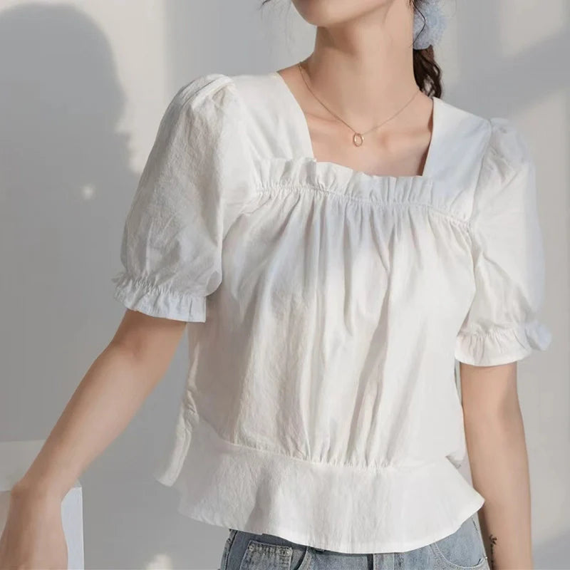 Une personne porte un chemisier blanc à manches courtes, à col carré et à manches bouffantes avec un ourlet à volants et un jean bleu - inspiration idéale pour le patron de couture gratuit pour chemisier à manches bouffantes de Longan Craft France. Une partie de la tête est hors cadre.