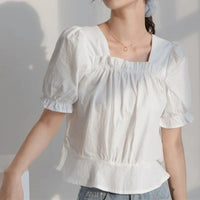 Une personne porte un chemisier blanc à manches courtes, à col carré et à manches bouffantes avec un ourlet à volants et un jean bleu - inspiration idéale pour le patron de couture gratuit pour chemisier à manches bouffantes de Longan Craft France. Une partie de la tête est hors cadre.