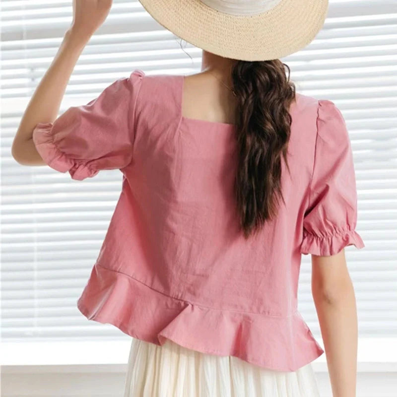 Une femme aux longs cheveux bruns attachés en queue de cheval porte le "Patron de couture gratuit pour blouse à manches bouffantes" de Longan Craft France, une blouse rose à col carré et à ourlet volanté, inspirée des modèles français chic PDF.