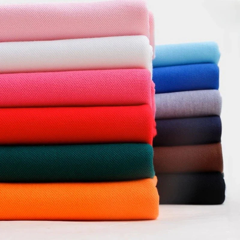 Une pile de tissu Longan Craft France piqué de coton uni au mètre dans des couleurs unies assorties - idéal pour les chemises et les polos - présenté sur un fond uni. Tissu jersey tricoté coton DIY pour couture.