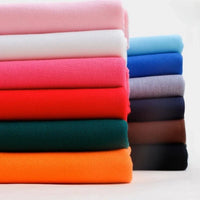 Une pile de tissu Longan Craft France piqué de coton uni au mètre dans des couleurs unies assorties - idéal pour les chemises et les polos - présenté sur un fond uni. Tissu jersey tricoté coton DIY pour couture.