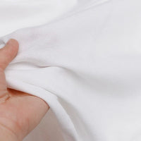 Une main étire un piqué de coton blanc et doux de Longan Craft France. Ce jersey léger et subtilement texturé est idéal pour les polos et les projets de couture de bricolage. Disponible au mètre comme "Piqué de coton uni" tricoté pour couture.