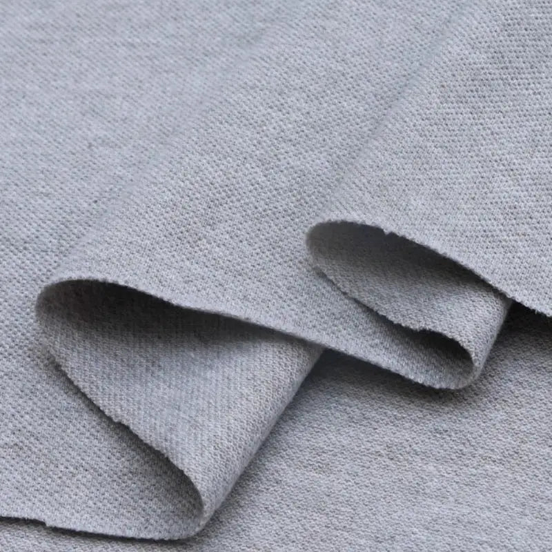 Un gros plan du Piqué de coton uni au mètre de Longan Craft France montre sa texture tissée gris clair, soigneusement pliée - parfait comme tissu piqué jersey pour les polos ou les projets de couture DIY.