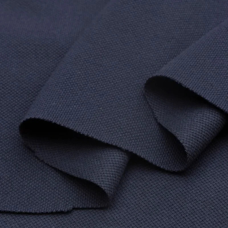 Gros plan sur le Piqué de coton uni au mètre de Longan Craft France - un tissu en jersey piqué bleu foncé avec un tissage texturé et visible, plié en couches pour mettre en valeur son épaisseur et sa structure. Idéal pour les polos et les projets de couture de bricolage.