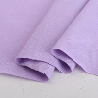 Gros plan sur le piqué de coton uni au mètre de Longan Craft France, un tissu de jersey tricoté violet clair soigneusement plié avec un motif tissé subtil - idéal pour les polos, les chemises et les projets de couture DIY.