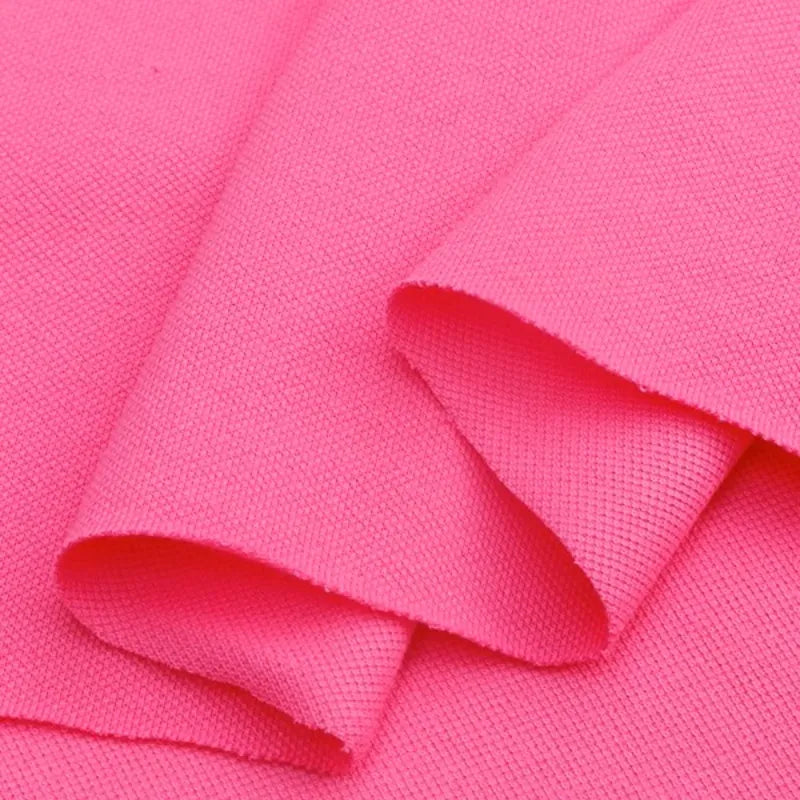 Gros plan sur le "Piqué de coton uni au mètre" rose vif de Longan Craft France, montrant plusieurs couches superposées avec un tissage texturé. Ce tissu piqué jersey pour polos semble doux, flexible et parfait pour les projets de couture DIY.