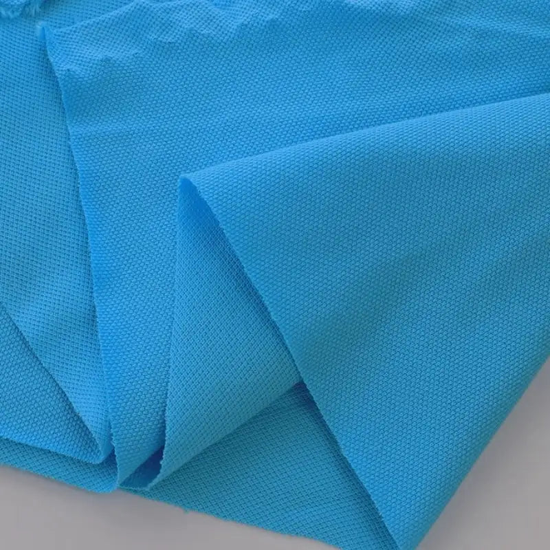 Plusieurs pièces de piqué de coton uni au mètre de Longan Craft France sont superposées sur une surface plane. Ce tissu en jersey de coton a un léger éclat et une texture semblable à celle d'une maille. Il est parfait pour coudre des polos ou des chemises.