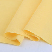 Gros plan sur deux pièces superposées de Piqué de coton uni au mètre jaune clair de Longan Craft France, montrant la surface texturée et tissée - parfait tissu piqué jersey pour polos et couture DIY.