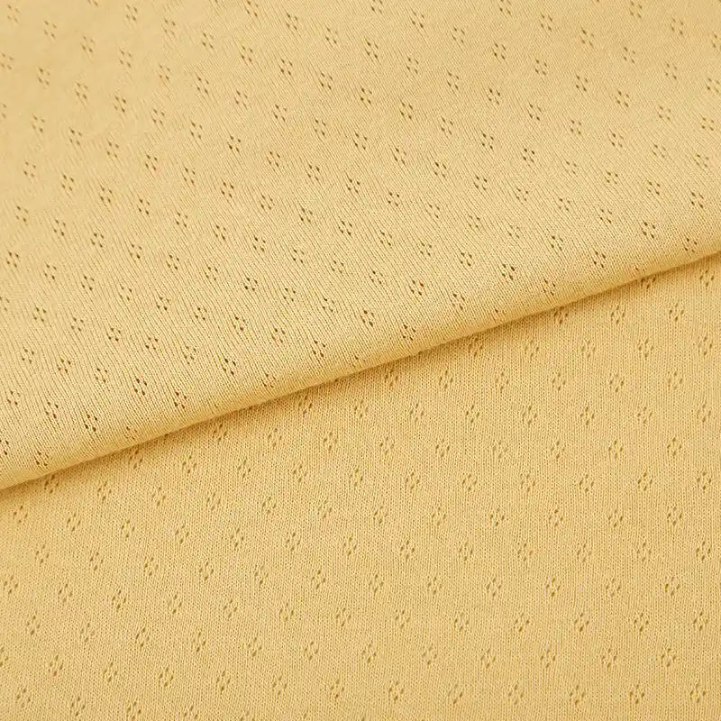 Gros plan sur le Tissu jersey pointelle 100% coton de Longan Craft France, un tissu jacquard pointelle jaune clair avec un petit motif en pointillés et un pliage diagonal visible - idéal pour confectionner des bodys pour bébé.