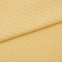 Gros plan sur le Tissu jersey pointelle 100% coton de Longan Craft France, un tissu jacquard pointelle jaune clair avec un petit motif en pointillés et un pliage diagonal visible - idéal pour confectionner des bodys pour bébé.