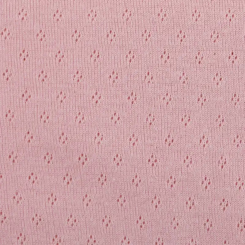 Un gros plan sur le Tissu jersey pointelle 100% coton de Longan Craft France montre son tissu jacquard doux et léger avec un motif ajouré à losanges répétés - un textile de bricolage parfait pour les bodys pour bébés, vendus au mètre.