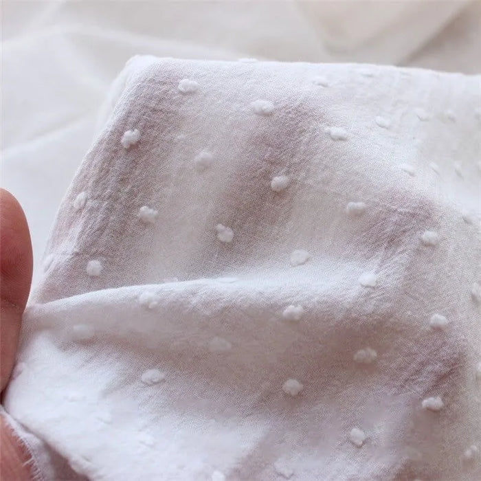Gros plan d'une main tenant Tissu plumetis 100% coton blanc pur de Longan Craft France, mettant en valeur sa texture à pois surélevés-parfait au mètre pour vêtements légers et décoration.