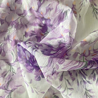 Gros plan sur le tissu mousseline imprimé fleurs de glycine violettes au mètre par Longan Craft France, révélant des plis doux et un imprimé floral délicat avec des fleurs de glycine violettes et des feuilles vertes sur un tissu léger et aéré.