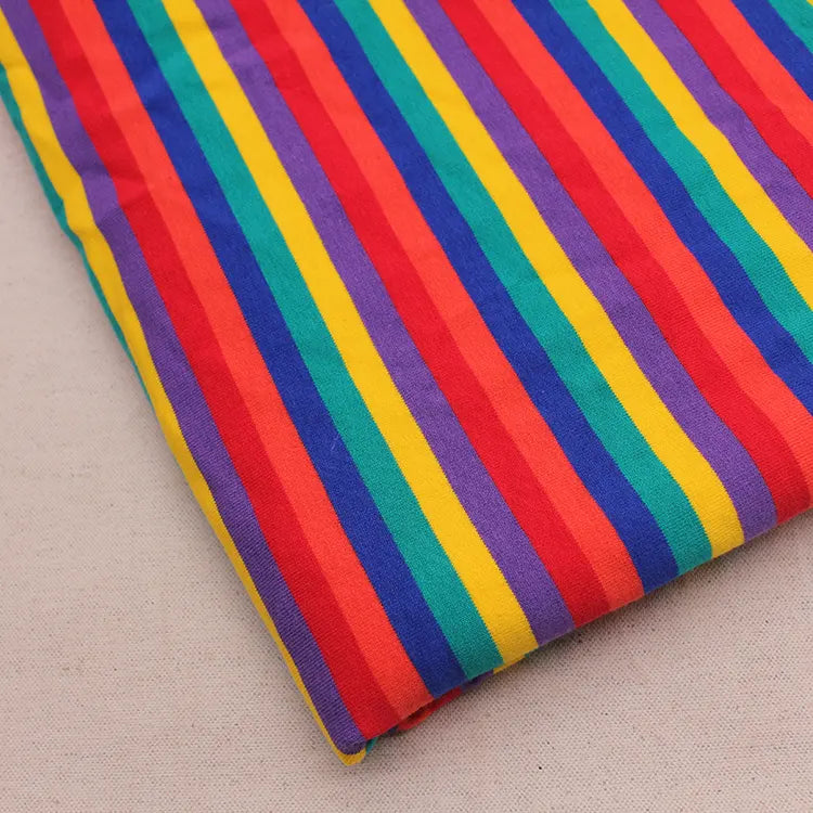 Un morceau de Longan Craft France Tissu French Terry extensible à rayures arc-en-ciel, un tricot de coton doux aux rayures verticales colorées, est présenté sur une surface beige clair.