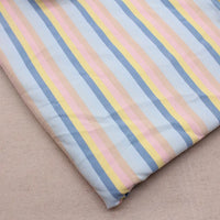 Un morceau plié de Longan Craft France Tissu French Terry extensible à rayures arc-en-ciel, présentant des rayures verticales bleues, jaunes, roses et beiges, est présenté sur une surface beige unie.