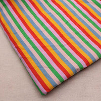 Un morceau de Longan Craft France Tissu French Terry extensible à rayures arc-en-ciel, présentant des rayures verticales régulièrement espacées en rouge, orange, jaune, vert, bleu et rose, est présenté sur une surface beige unie.