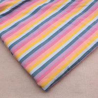 Un morceau de Longan Craft France Tissu French Terry extensible à rayures arc-en-ciel (coton tricoté, doux) est plié sur une surface beige, mettant en valeur ses rayures diagonales roses, jaunes, blanches et bleues.