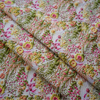 Gros plan sur le "Tissu brocart rétro floral au mètre" de Longan Craft France, un tissu d'ameublement jacquard avec des broderies botaniques rétro colorées - feuilles vertes, fleurs roses, jaunes, orange et blanches - sur un fond clair, légèrement plié.