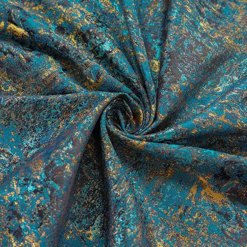 Gros plan sur Tissu brocart vert rétro au mètre de Longan Craft France, un tissu d'ameublement jacquard aux accents métalliques dorés et aux plis tourbillonnants dans des motifs marbrés bleu sarcelle, or et marron foncé.