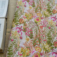 Gros plan sur le Tissu brocart rétro floral au mètre de Longan Craft France, un jacquard brodé d'ameublement avec des motifs roses, jaunes et verts, présenté sur un journal à côté d'un livre ouvert.
