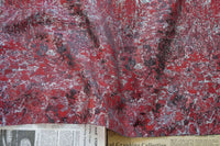 Un morceau de Tissu brocart vert rétro au mètre de Longan Craft France est drapé sur un journal partiellement visible avec du texte et des petites annonces au bas de l'image.