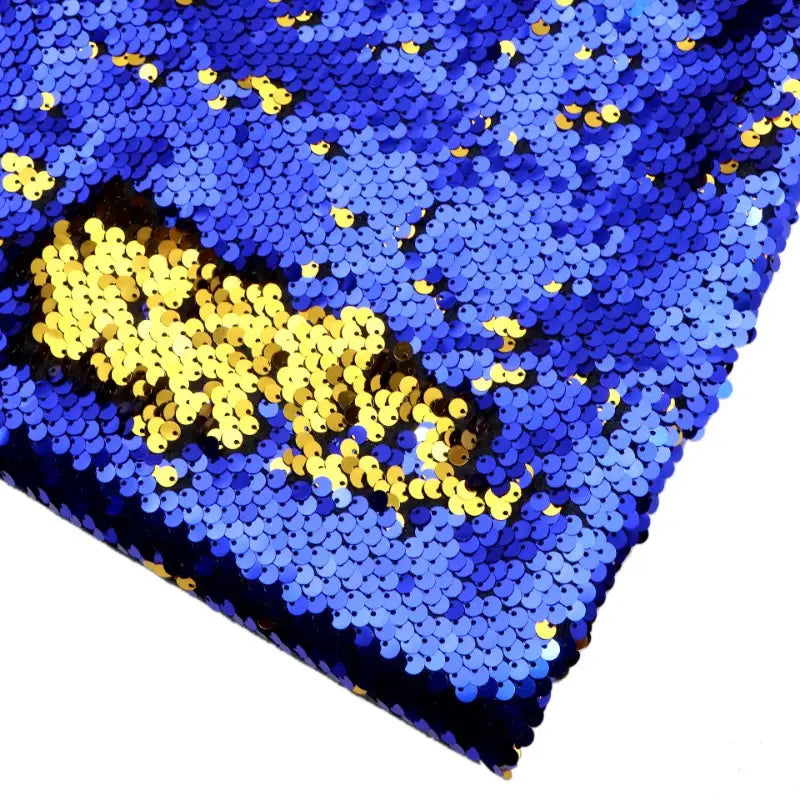Gros plan sur le tissu pailleté bicolore réversible au mètre de Longan Craft France, composé principalement de paillettes bleues avec une section dorée pour un aspect brillant et texturé qui met en valeur son effet pailleté réversible - idéal pour les accessoires.