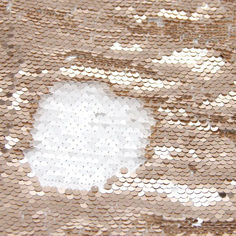 Un gros plan de Tissu pailleté bicolore réversible au mètre, de Longan Craft France, montre sa surface texturée et scintillante : des sequins or brossés révèlent du blanc dessous pour un effet contrasté idéal pour accessoires.